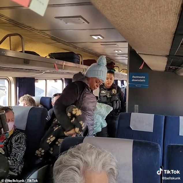 One of the women collecting her belongings as she exits the train while an officer stands by.