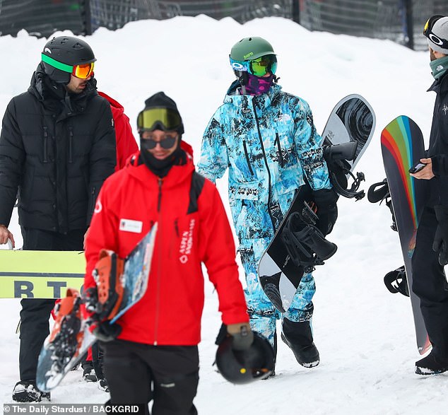 In the company: The megastar appeared on the sparkling white mountain, surrounded by an entourage of fellow snowboarders dressed in black and red.