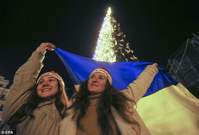 Ukrainians hold the Ukrainian national flag near a Christmas tree at night in Kyiv, Ukraine, on December 31, 2022.