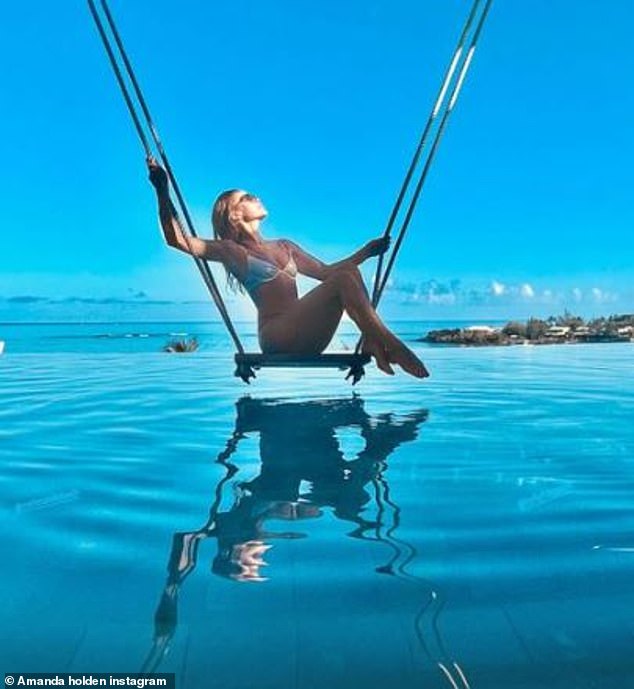 Stunning: The 51-year-old TV personality took to Instagram to share a snapshot of herself in a skimpy bikini as she sat on a swing and dunked her toned legs in the pool at the luxurious five-star hotel  Amanda looked amazing in the barely there skimpy bikini that consisted of a white triangle bikini top and a pair of skimpy thong bikini bottoms.