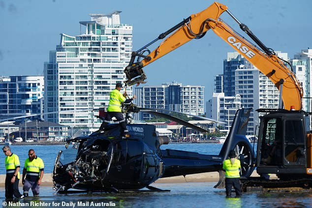 The wrecked remains of the helicopter are being lifted from the sandbar.