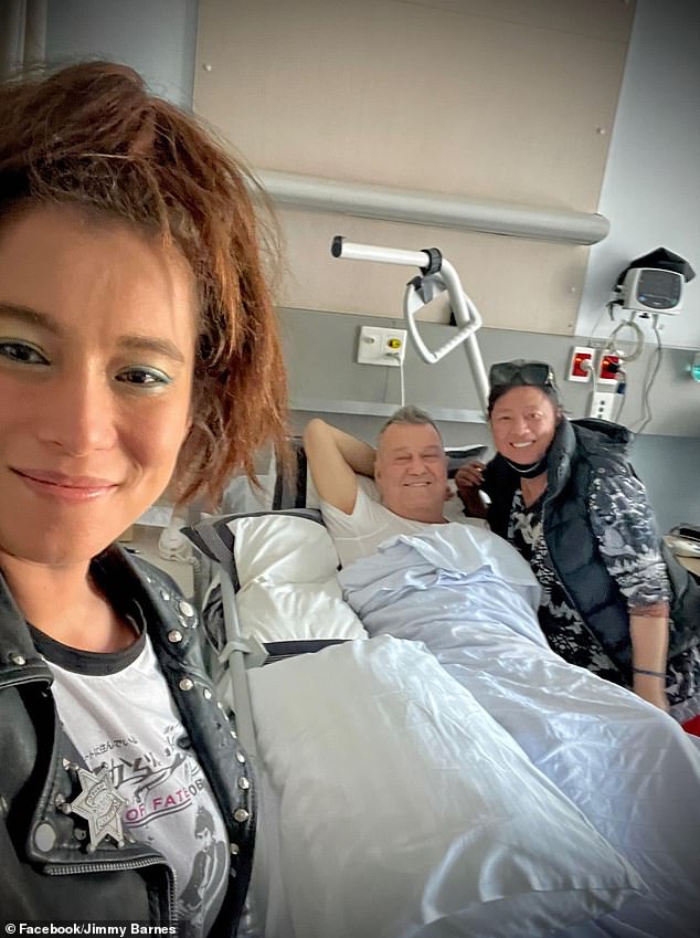 Last month, Jimmy Barnes updated his fans as he recovered in the hospital following urgent hip surgery.  In an update shared on Facebook, the 66-year-old rocker was convalescing in his hospital bed with his wife Jane, 66, and his daughter Elly-May Barnes, 33. All pictured.