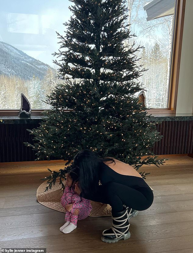 Cozy: Stormi sat in front of a giant Christmas tree as Jenner leaned in and hugged her in a black cotton catsuit