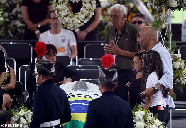 The Brazilian star died on December 29 at the age of 82 after a long battle against cancer, and was mourned this Monday and Tuesday at the stadium of his former club Santos, where thousands of people came to see him off.  Pictured: Pele's son Edinho stands with mourners as the body of Brazilian soccer legend Pele is seen in his coffin as he lay on the field of his former club Santos' Vila Belmiro stadium.