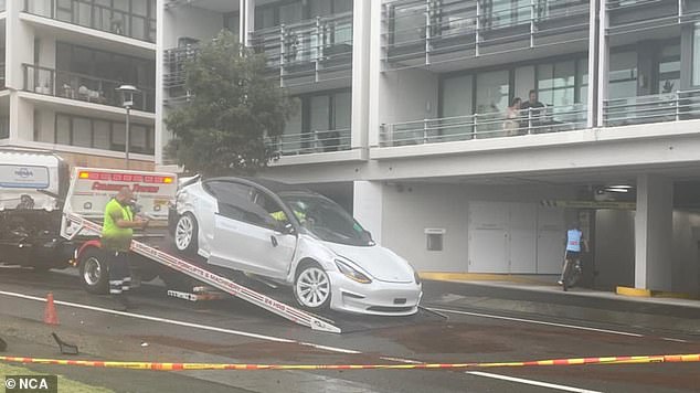 The crashed Tesla is shown being transferred to a truck for removal from the scene.