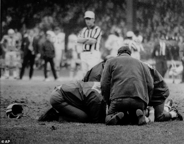 While the helmet of Detroit Lions wide receiver Chuck Hughes sits near the spot where he fell in the last minute of a game on October 25, 1971, between the Lions and the Chicago Bears, team physician Edwin Gis, leaning over Hughes, on the right.  Hughes, 28, had just finished a passing pattern when he tripped and fell.  He later died at a Detroit hospital.