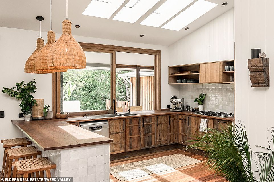 A dining area sits below a service window that opens to the terrace, while natural light pours into the kitchen through the overhead skylight that features smooth wood benchtops, rustic wood cabinets, and an outdoor bar. adjoining outdoors.