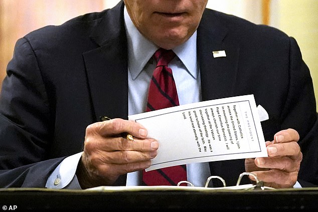 President Joe Biden holds up a card after signing a book of condolences for the late Pope Benedict Thursday night in Washington.