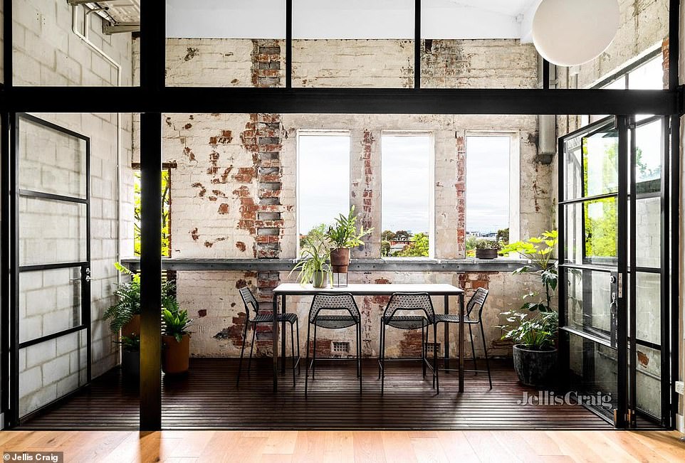 Bi-fold glass doors retract to extend the dining area onto a terraced balcony and outdoor entertaining area lined with weathered brick walls