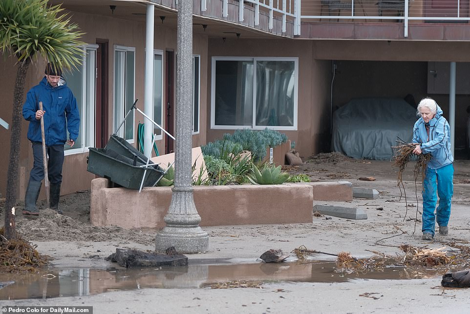 A couple cleans up debris outside their home on Thursday.  More than 40,000 Californians still without power