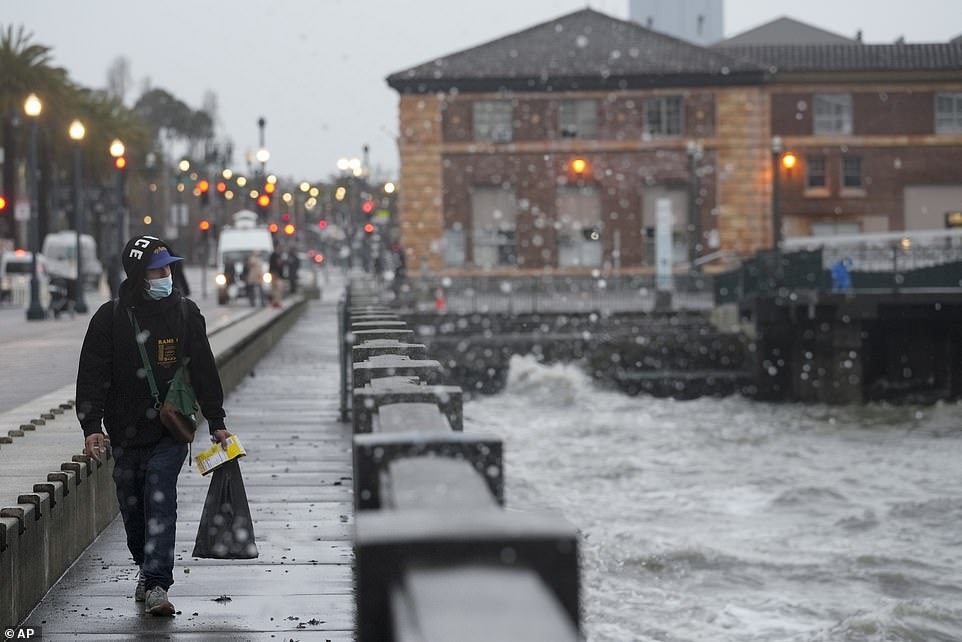 A man walks across a bridge at high tide in San Francisco.  The city is expected to receive more rain today after a week of heavy rain