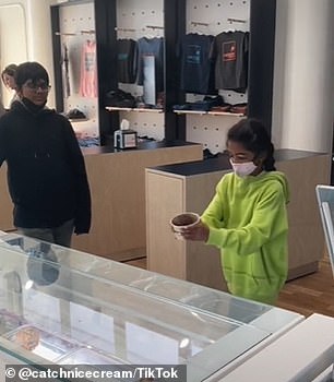 A boy extends his cup to catch a scoop of ice cream.