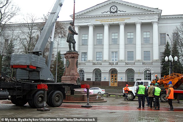 Some of the workers climbed onto a crane as a crane lowered a large strap to wrap around the monument to the scientist.  Others cordoned off the area from other locals