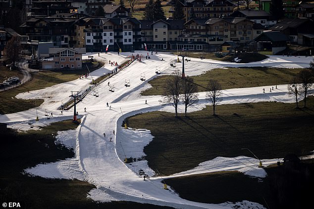 Skiers go down a slope in a snowless part of Schladming, Austria