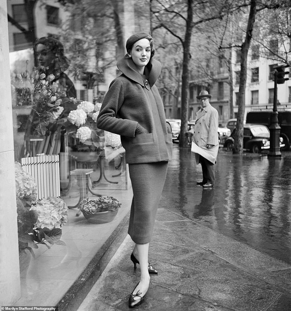 Ready-to-wear on a rainy day: Marilyn Stafford captured this image in Paris in 1960. It shows a woman on the streets of Paris on a rainy day.  Her silhouette is reflected in a shop window.