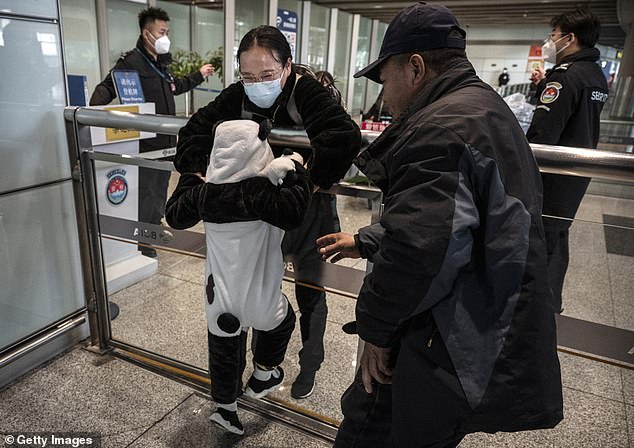 A woman lifts a young relative dressed in a panda suit over a barrier to hug him as he arrives from a flight at the international arrivals area of ​​Beijing Capital Airport after restrictions were lifted today.