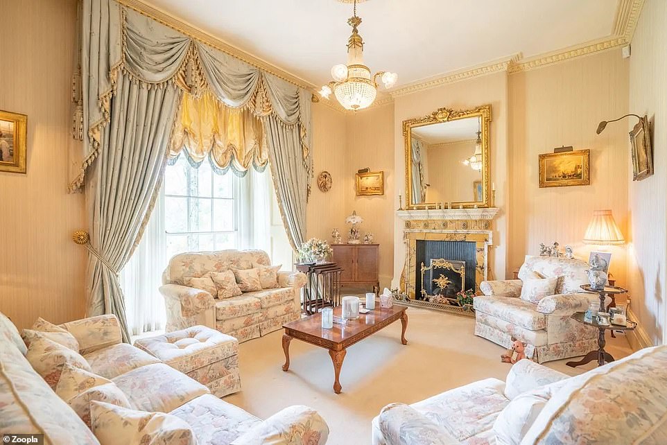 The home has a lavish interior, including this gold-colored living room with sheer curtains and a large fireplace