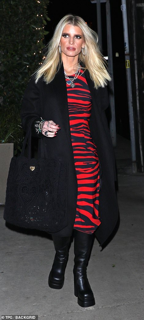 On trend: The singer opted for a red and black striped dress that clung to her toned frame along with a long coat and chunky boots