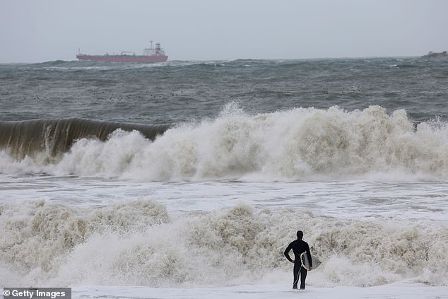 On Saturday, a surfer watches the big waves caused by the storm surge