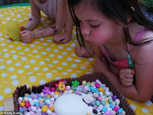 She blows out the candles on her birthday cake during a family garden party for her sixth birthday