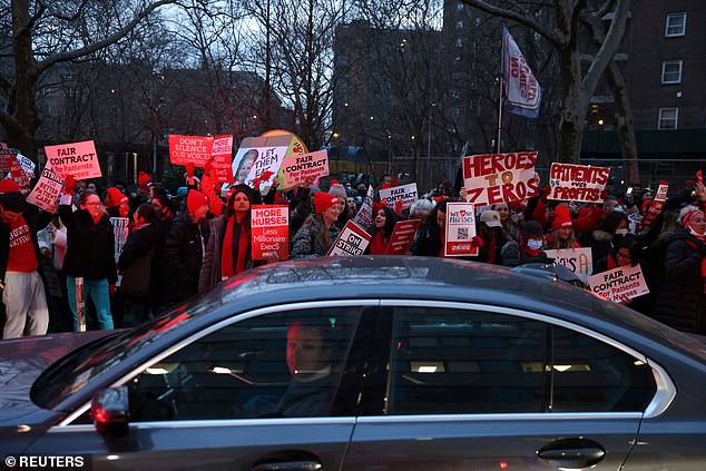 A morning commuter walks past a large group of nurses who went on strike in New York City on Monday.