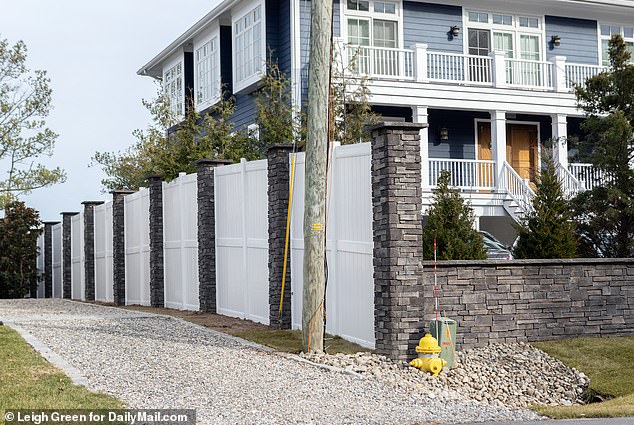 Tall white portions of the non-see-through fencing are broken-up by gray stone pillars lining the sidewalk