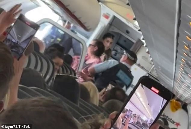 A passenger who uploaded the images to TikTok told viewers that the three-hour flight had been delayed by an hour because of the ordeal (in the photo, police officers carry the woman out)