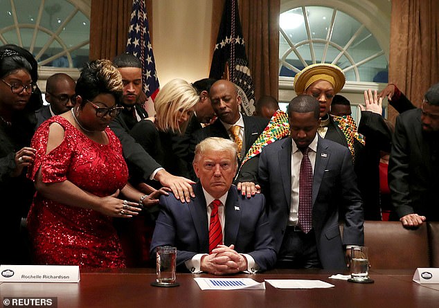 African-American supporters, including Terrence Williams, Angela Stanton, and Diamond and Silk, pray with US President Donald Trump in the Cabinet Room of the White House in February 2020.