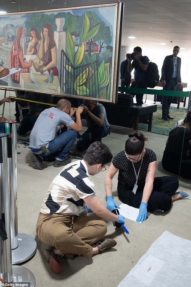 Employees specializing in the conservation of works of art sit near a painting by painter Emiliano Di Cavalcanti that was destroyed by radical supporters of former President Jair Bolsonaro after a riot the previous day at the Planalto Palace in Brasilia, Brazil.