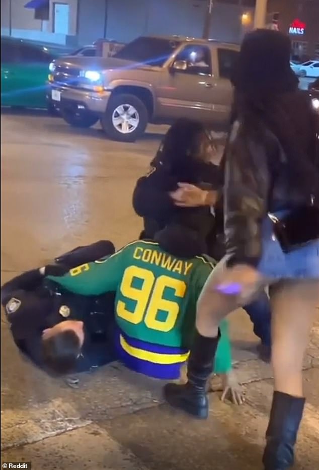 As they drop to the ground and struggle, at least one man in a Chiefs sweatshirt tries to throw a punch at one of the guards.