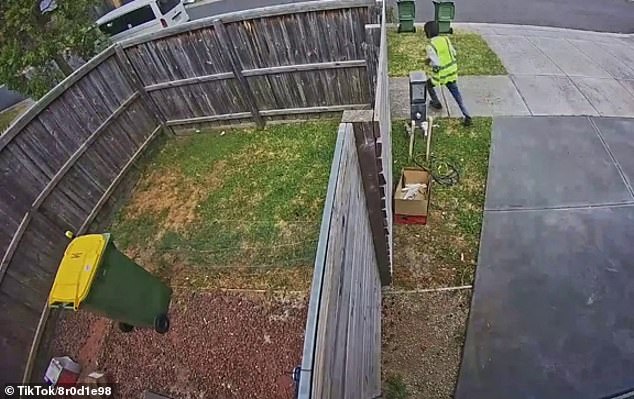 The box lands on a gravel driveway and falls on its side as the courier, wearing a high-visibility vest, runs away from the residence and down the street.