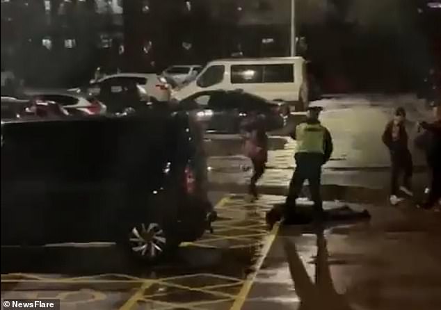 Police officers can be seen standing over the man, who is lying face down on the ground in the parking lot, before walking away.