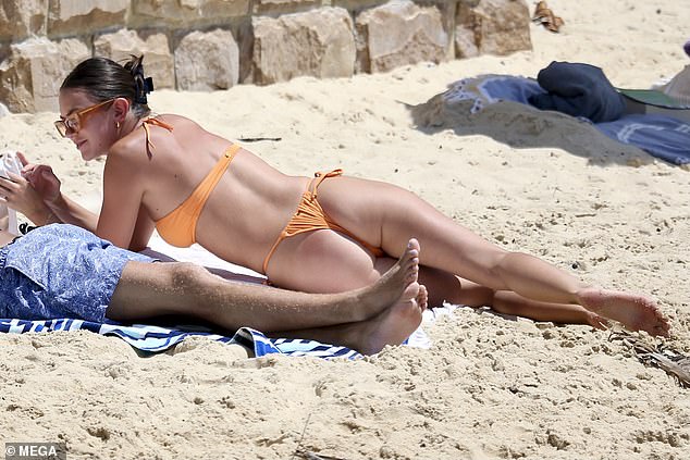 The 24-year-old fashion student flaunted her toned physique in a skimpy orange bikini while relaxing on the sand with a friend.