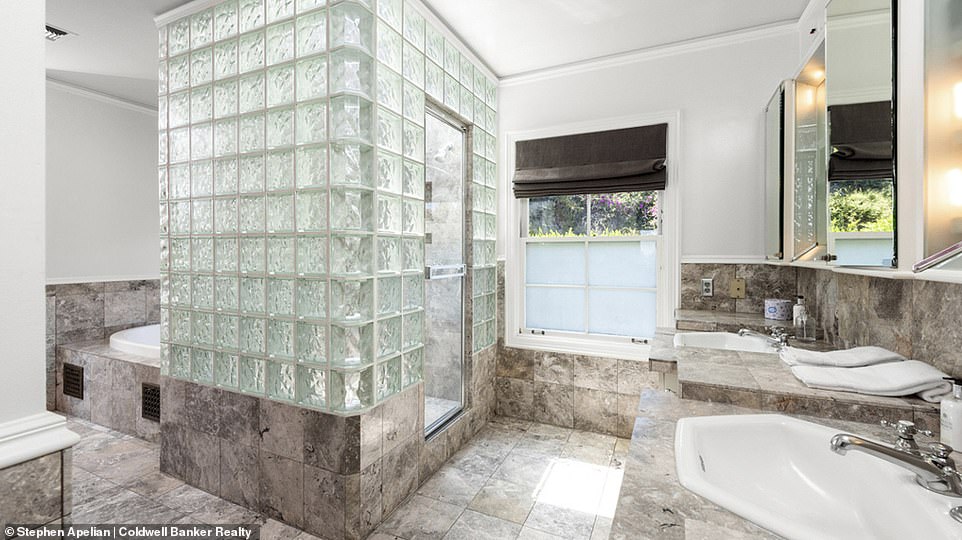 Another of the property's bathrooms, featuring an art deco glass tiled walk-in shower leading to a sunken bath, with his and her sinks.