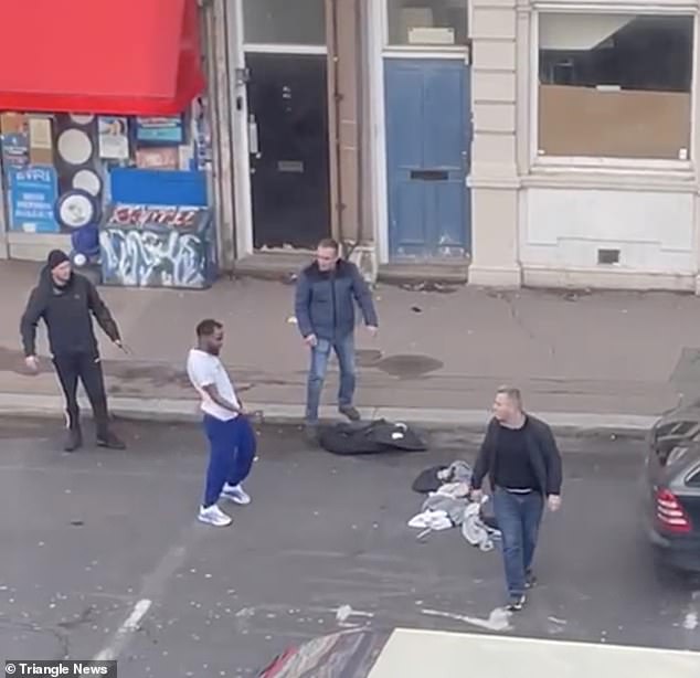 At the beginning of the video, the driver's friend appears to be returning to his car when the pedestrian, dressed in a white T-shirt and blue sweatpants, makes a lewd gesture.