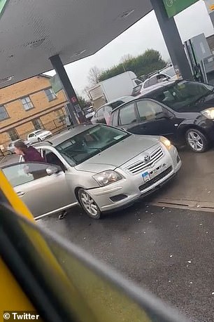 The woman, wearing a purple raincoat, is seen storming out of her car while screaming at the other female driver, before throwing a drink at the black Ford at the petrol station