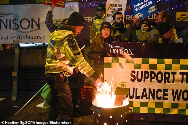 An ambulance worker lights a camp fire to combat the cold while on strike outside their base at Waterloo in London on Wednesday