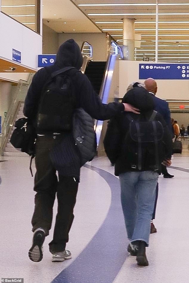 Showing Support: He placed a comforting hand on her back as they strolled through the transportation hub.