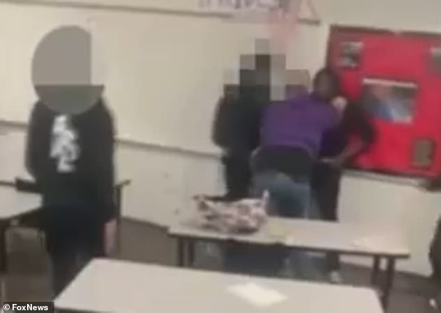 The teacher held the struggling student against the wall with his hands on either side of his neck, while a group of other students seemed to try to separate them.