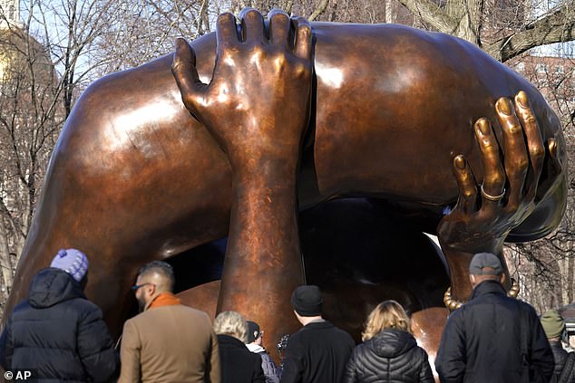 People stand near the 20-foot-tall bronze sculpture. "Hug," a memorial to Dr. Martin Luther King Jr. and Coretta Scott King, on the Boston Common