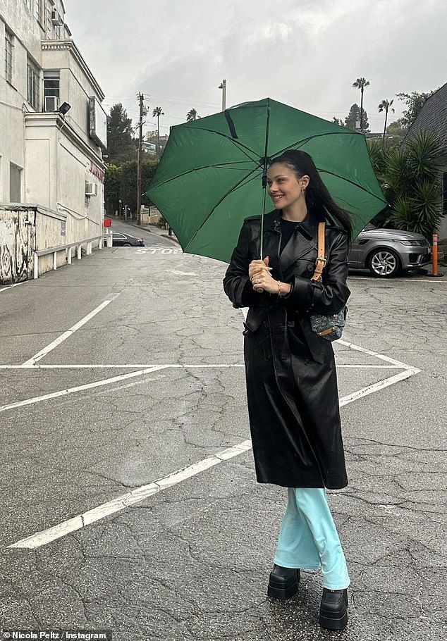 Stunning: Nicola looked effortlessly chic in a black leather trench coat, teamed with blue jeans and chunky boots as she posed with a green umbrella