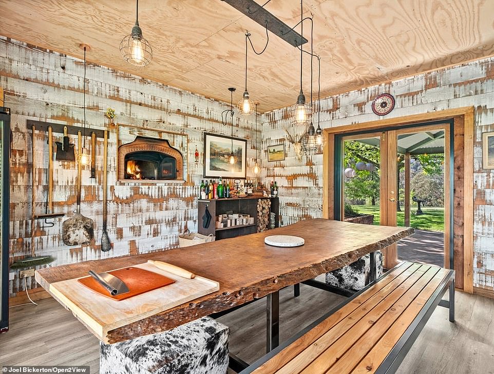 A modern, white kitchen contrasts with the country-style pizzeria next to the dining area with a wood-burning oven, wooden ceiling, benches and a fridge