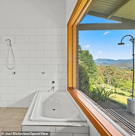 In the master bath, a luxe soaking tub sits below a large window that overlooks the landscape and outdoor shower.