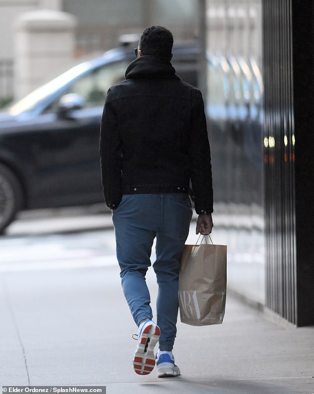 Holmes walks away down a New York City sidewalk with a Zara bag in one hand.