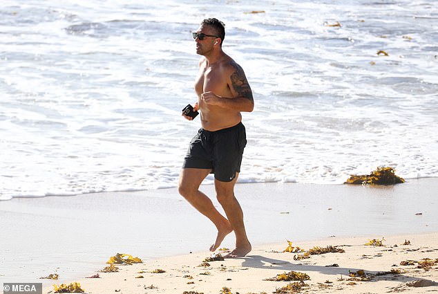 The former Roosters player showed off his biceps, complete with tattoos on his left arm, as he ran across wet and dry sand