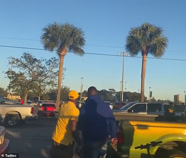 A man (pictured) can even be seen holding a black handgun as he looks across the parking lot and partially hides behind a pickup truck.