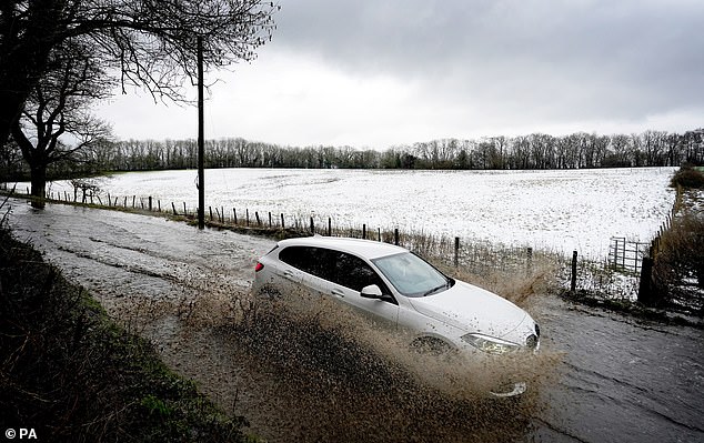 A car passes through floodwaters next to a snow-covered field near Wrotham in Kent on Monday