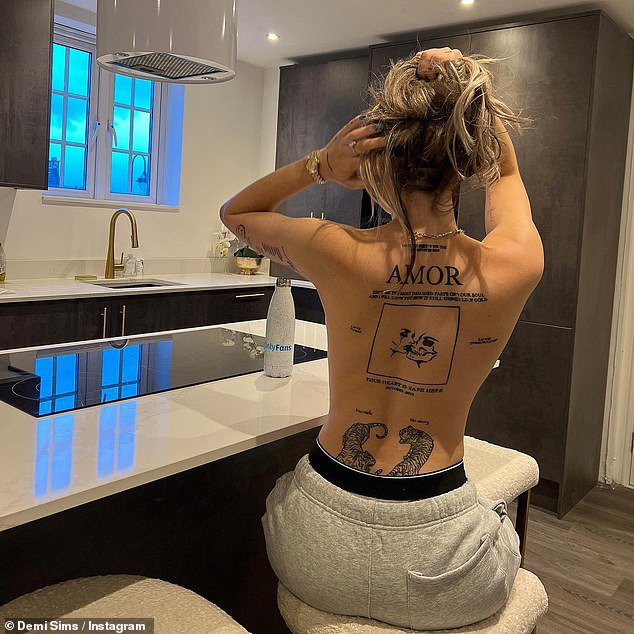 Stunning: Demi held up her long blonde locks to show off her already tattooed back as she sat at a breakfast bar in her kitchen