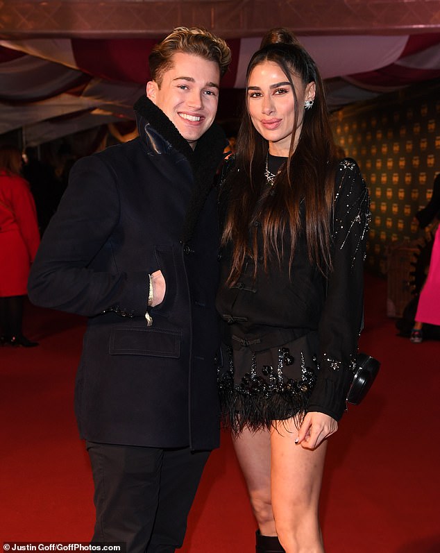 Coordinated: AJ cut a casual figure in a dark coat and scarf, while Zara opted for a stunning dark minidress and statement designer leather knee-high socks as they posed for the cameras