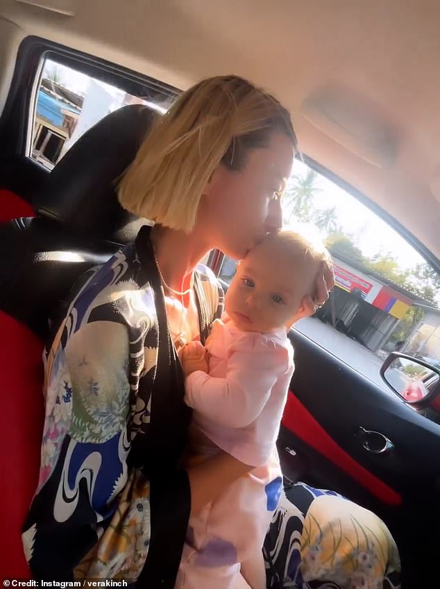 The baby is not wearing a seatbelt and Anna holds him by the open car window.